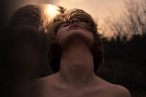 Mulher madura de olhos fechados, respirando fundo em um ambiente de luz e sombra, transmitindo a paz de voltar para a sua essência e resgatar a própria identidade.